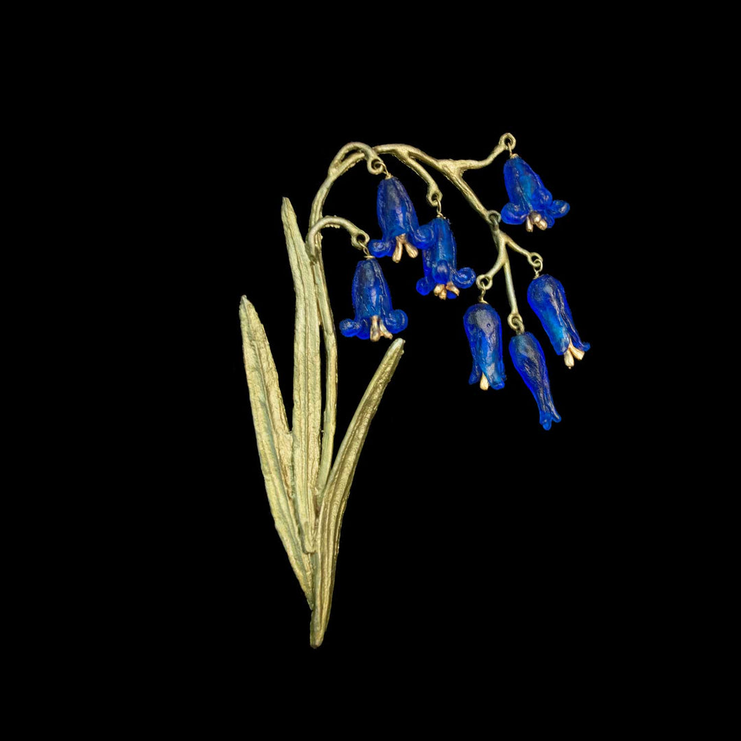 Eine grünfarbene Blumenbrosche mit baumelnden blauen glockenförmigen Blüten und länglichen Blättern auf schwarzem Hintergrund.