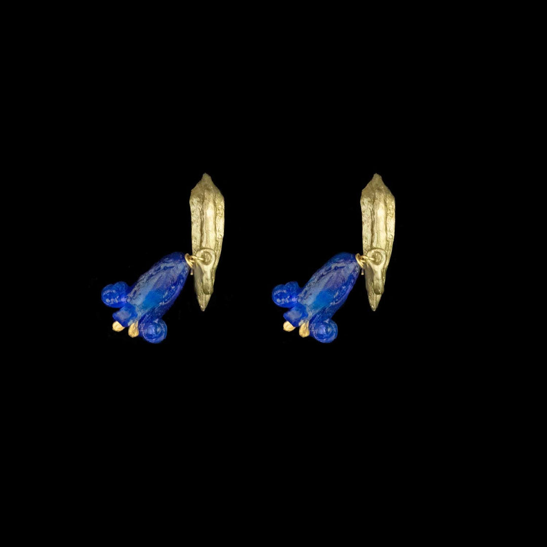 Ein Paar grüne Ohrstecker mit jeweils einer baumelnden blauen Glasblüte vor schwarzem Hintergrund.