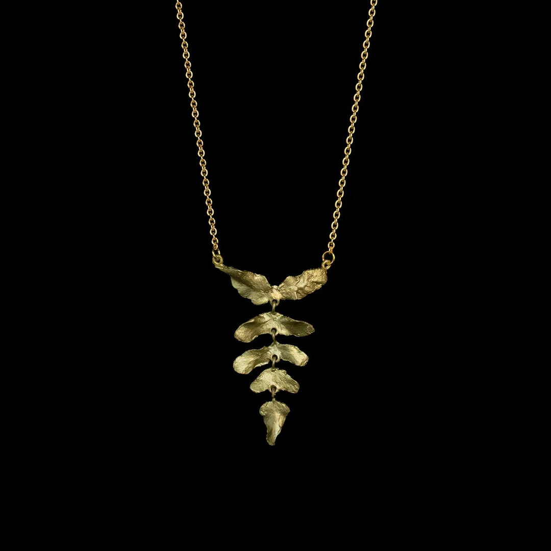 Ein grüner Blattanhänger an einer zarten Goldkette vor schwarzem Hintergrund.