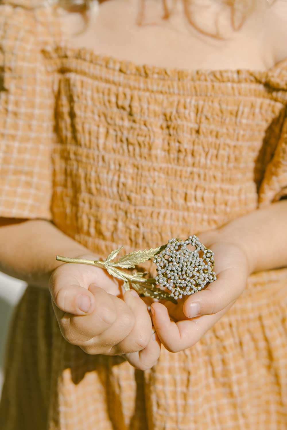 A child in an orange dress is holding the queen anne's lace brooch in her hand. Focus is on the hands, with the girl only partly visible.