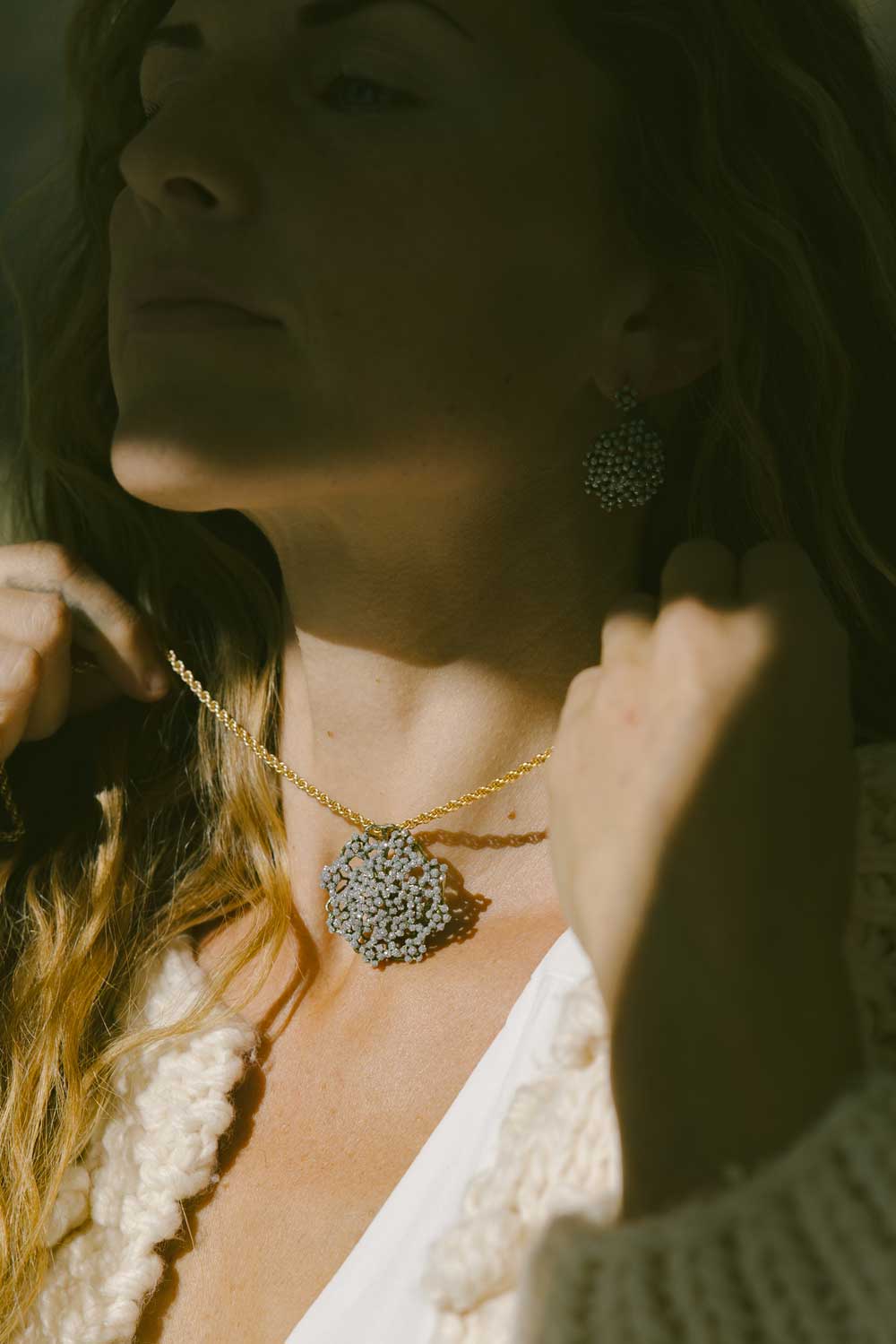 A woman putting on a golden twist necklace with a large round sparkly pendant.